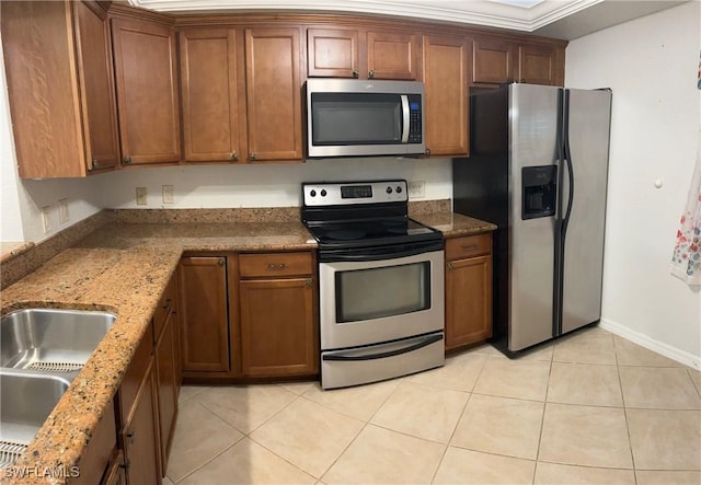 kitchen with brown cabinets, a sink, appliances with stainless steel finishes, light tile patterned floors, and stone counters