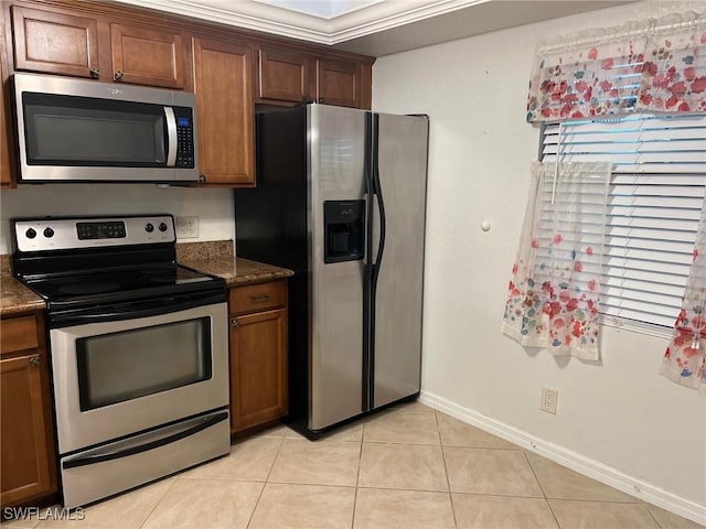 kitchen featuring light tile patterned floors, brown cabinets, appliances with stainless steel finishes, and baseboards