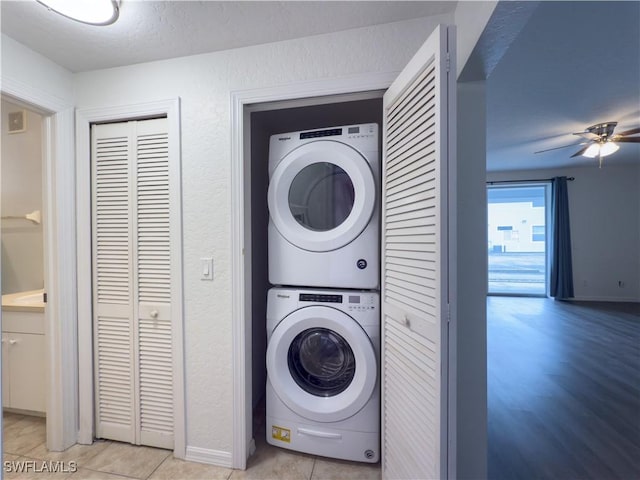 laundry area featuring baseboards, light tile patterned floors, laundry area, stacked washer / drying machine, and a ceiling fan