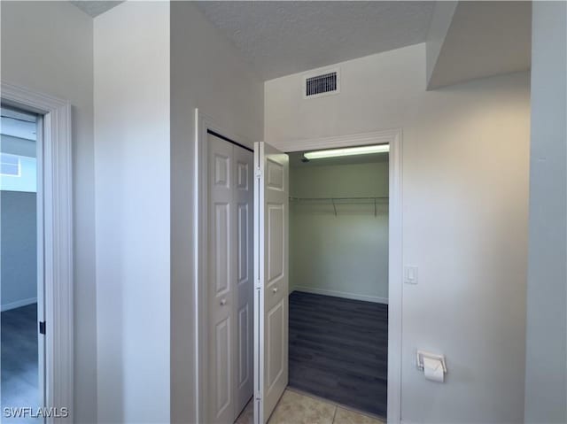 hallway with light tile patterned floors, visible vents, baseboards, and a textured ceiling