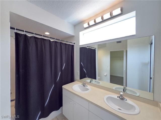 full bath featuring a textured ceiling, double vanity, and a sink