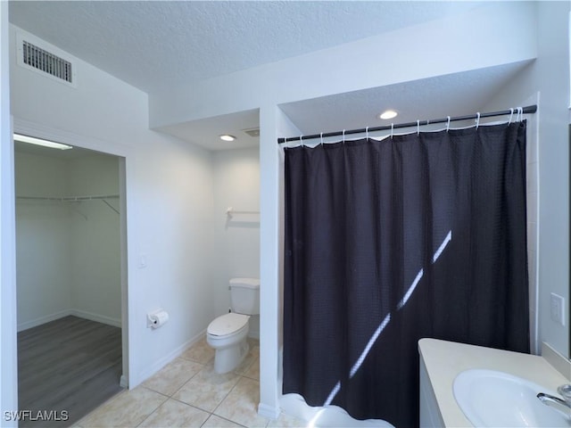 bathroom featuring tile patterned flooring, visible vents, a walk in closet, toilet, and a textured ceiling