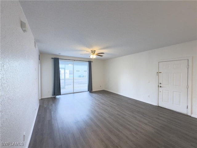 unfurnished room featuring baseboards, dark wood-type flooring, ceiling fan, and a textured wall