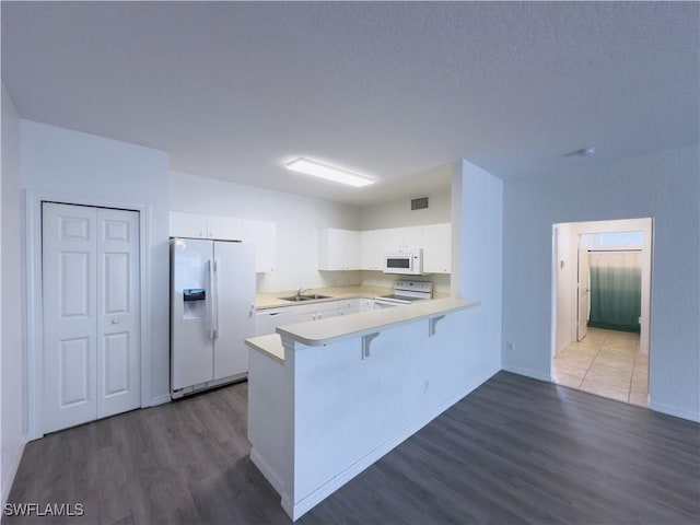 kitchen with a sink, white appliances, a peninsula, white cabinets, and light countertops