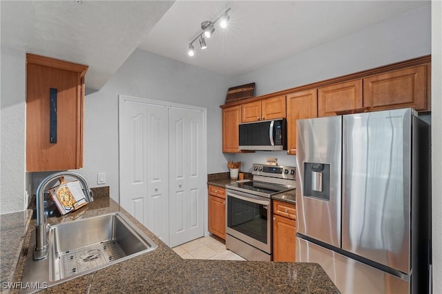 kitchen with light tile patterned floors, brown cabinets, stainless steel appliances, and a sink