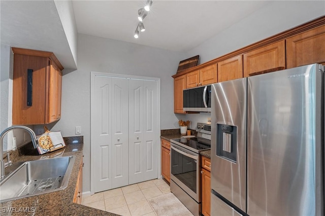 kitchen with brown cabinets, a sink, dark stone counters, appliances with stainless steel finishes, and light tile patterned floors