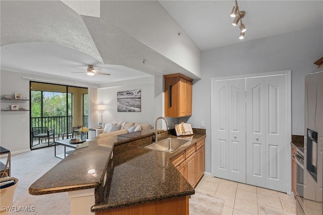 kitchen featuring a peninsula, dark stone counters, ceiling fan, a sink, and open floor plan