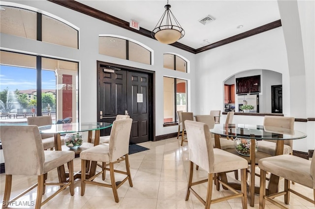 dining room with visible vents, baseboards, ornamental molding, a towering ceiling, and light tile patterned flooring