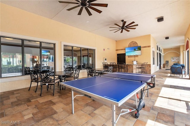 playroom featuring arched walkways, ceiling fan, and stone finish floor