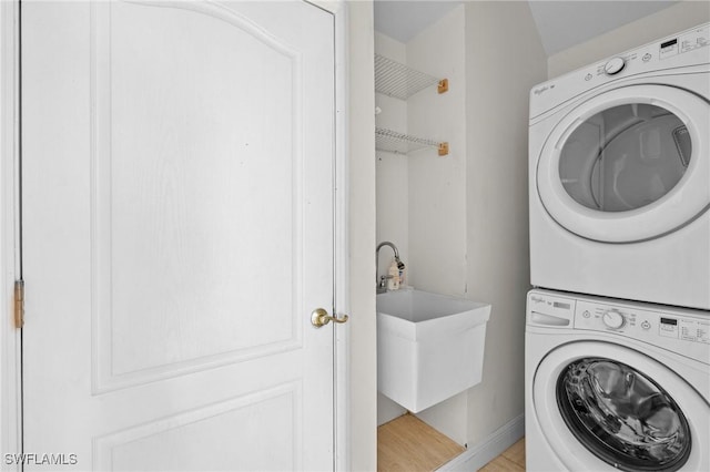 clothes washing area featuring baseboards, laundry area, a sink, stacked washer / dryer, and light wood-type flooring