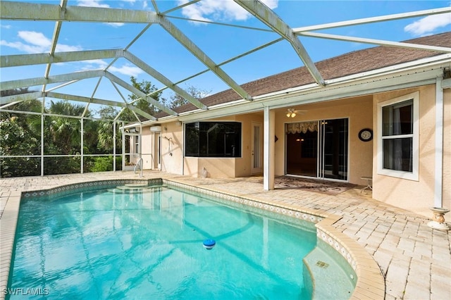 outdoor pool featuring glass enclosure, a ceiling fan, and a patio area