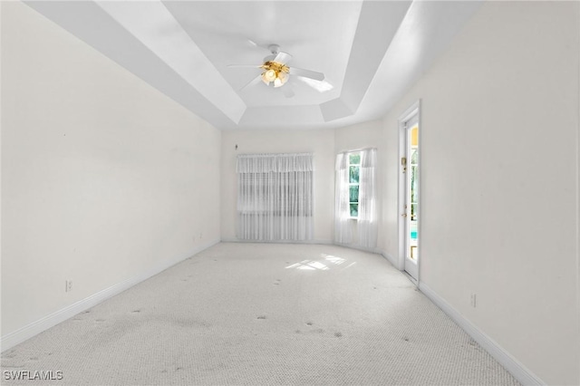 carpeted empty room with a tray ceiling, a ceiling fan, and baseboards