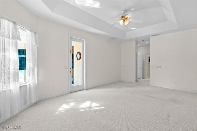 empty room featuring a tray ceiling, plenty of natural light, carpet floors, and baseboards