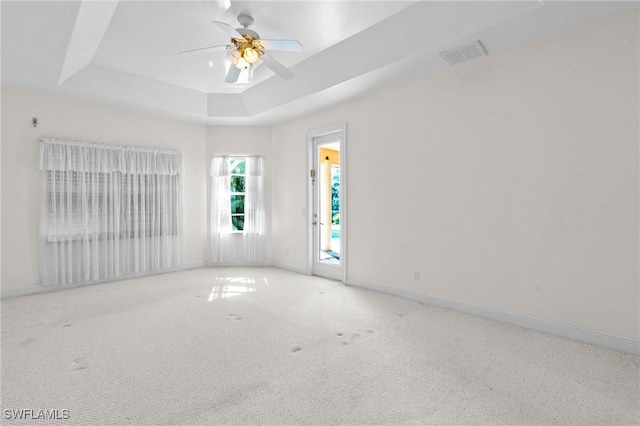 carpeted spare room with visible vents, baseboards, a raised ceiling, and ceiling fan