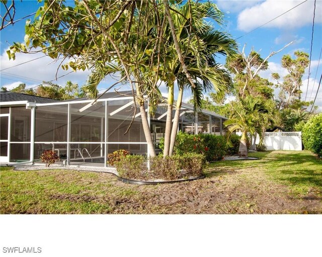 rear view of house featuring a lanai, a yard, and fence