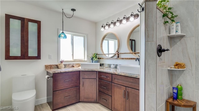 bathroom featuring double vanity, toilet, tiled shower, and a sink