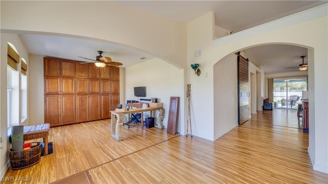 home office with arched walkways, light wood-style flooring, and a ceiling fan