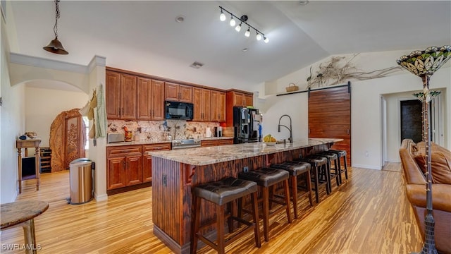 kitchen featuring lofted ceiling, light wood-style floors, black microwave, a kitchen bar, and refrigerator with ice dispenser