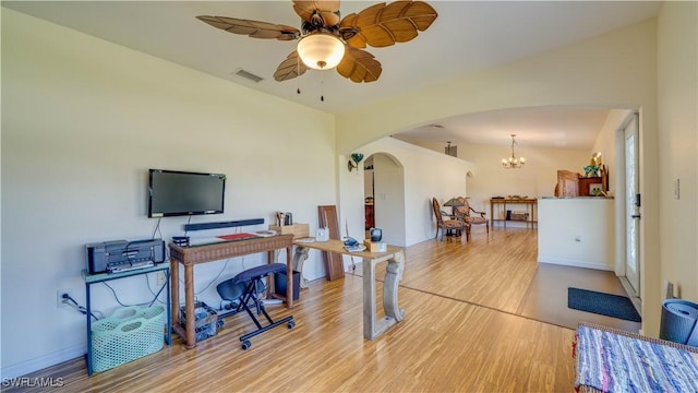 office featuring ceiling fan with notable chandelier, light wood-style flooring, arched walkways, and visible vents