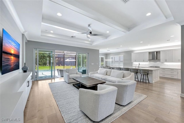 living area with recessed lighting, a raised ceiling, light wood-style flooring, and ceiling fan