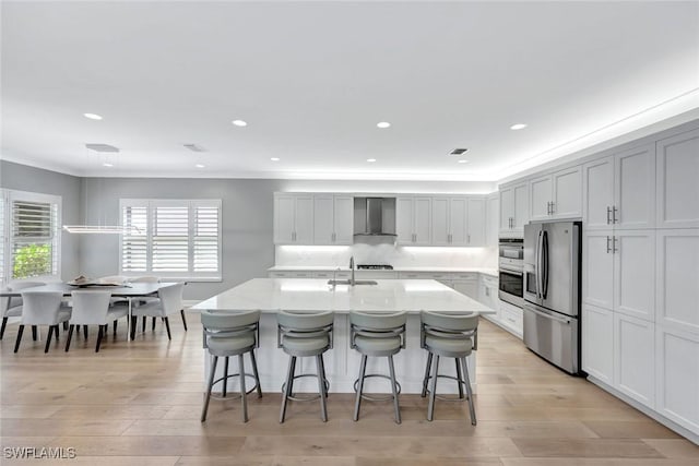 kitchen featuring light wood finished floors, a breakfast bar, light countertops, stainless steel refrigerator with ice dispenser, and wall chimney range hood