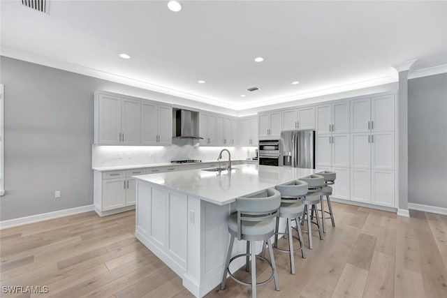 kitchen featuring a sink, ornamental molding, stainless steel appliances, wall chimney exhaust hood, and light wood-type flooring