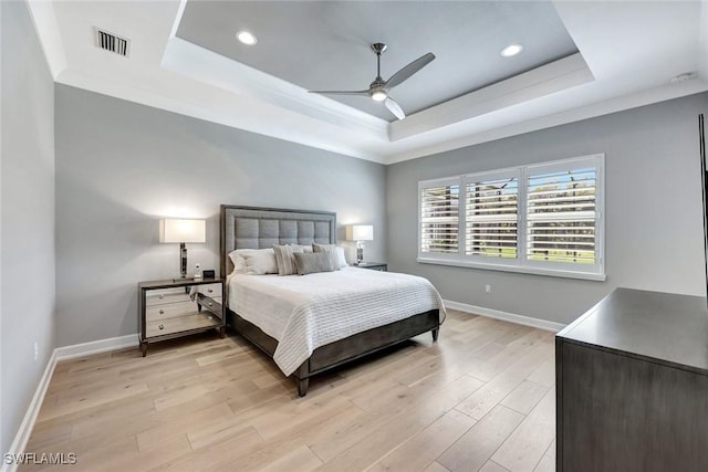 bedroom with baseboards, a raised ceiling, and light wood-style flooring