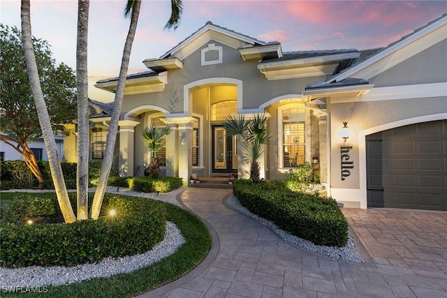 view of front of home featuring decorative driveway, french doors, an attached garage, and stucco siding