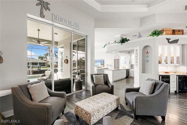 living area featuring beverage cooler, a tray ceiling, ornamental molding, dark wood-type flooring, and a dry bar