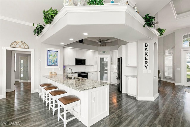 kitchen featuring a sink, white cabinetry, freestanding refrigerator, arched walkways, and a peninsula