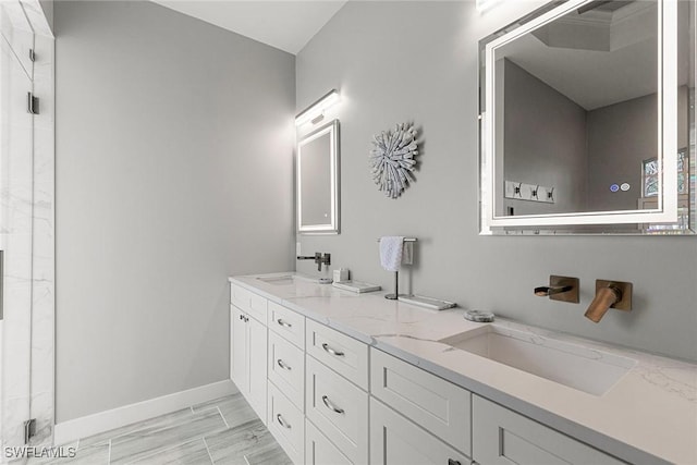 full bath with double vanity, a shower stall, baseboards, and a sink