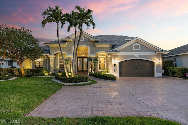 mediterranean / spanish-style house with a yard, stucco siding, french doors, a garage, and decorative driveway