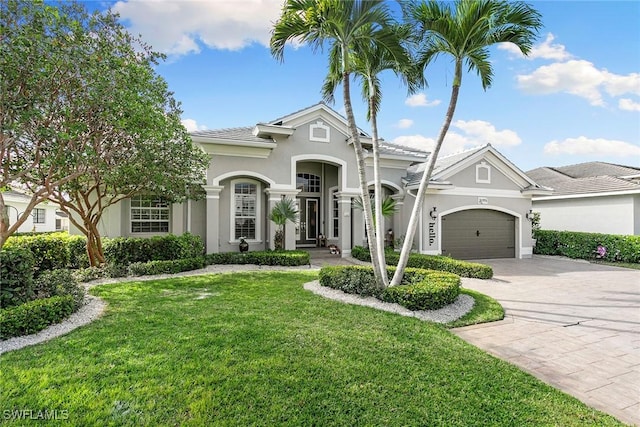 mediterranean / spanish house featuring decorative driveway, a garage, a front yard, and stucco siding