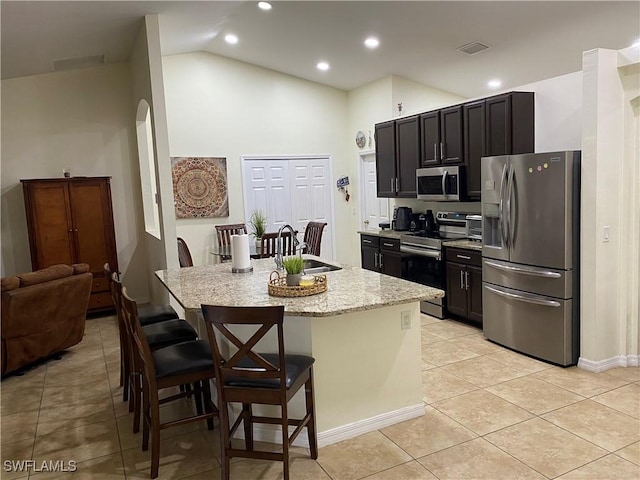 kitchen featuring a breakfast bar area, light tile patterned floors, a center island with sink, visible vents, and stainless steel appliances