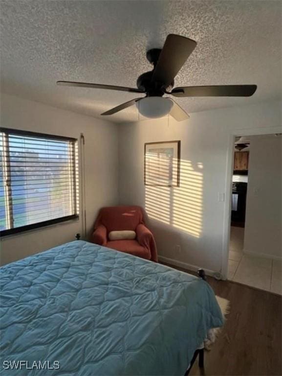 bedroom with a textured ceiling, multiple windows, wood finished floors, and ceiling fan