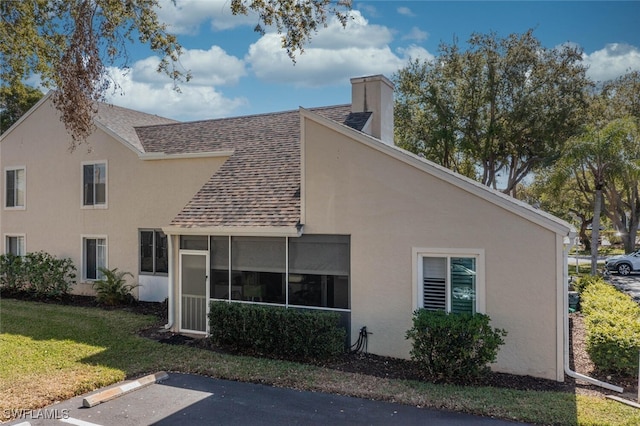 rear view of property with stucco siding, a lawn, a chimney, and a shingled roof