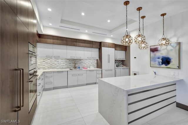 kitchen featuring oven, decorative backsplash, white cabinets, a raised ceiling, and a sink