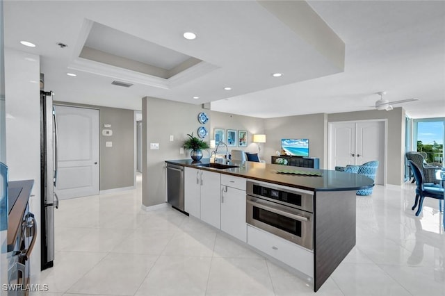 kitchen featuring a tray ceiling, a sink, stainless steel appliances, white cabinetry, and dark countertops