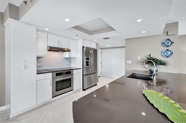 kitchen with dark countertops, under cabinet range hood, appliances with stainless steel finishes, white cabinetry, and a sink