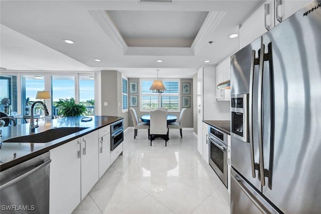 kitchen featuring dark countertops, stainless steel appliances, white cabinetry, a raised ceiling, and a sink