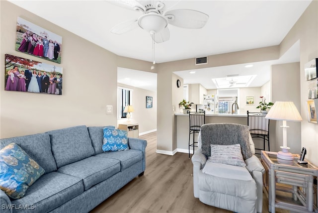 living area with visible vents, a ceiling fan, wood finished floors, a skylight, and baseboards