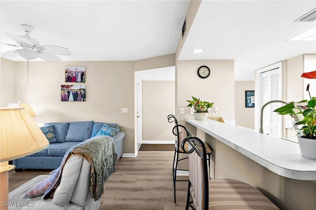 living room with ceiling fan, visible vents, baseboards, and wood finished floors