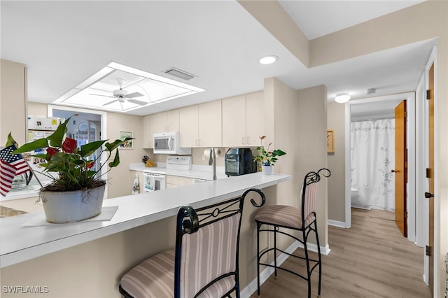 kitchen featuring white appliances, a breakfast bar area, visible vents, a skylight, and light countertops