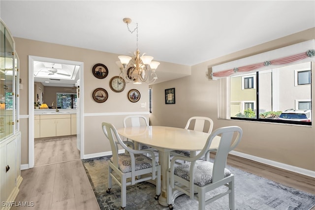 dining space with ceiling fan with notable chandelier, light wood-type flooring, and baseboards