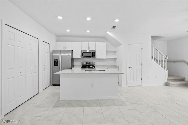 kitchen with a center island with sink, open shelves, white cabinetry, stainless steel appliances, and light countertops