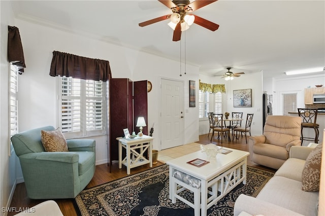 living area featuring baseboards, wood finished floors, ceiling fan, and crown molding