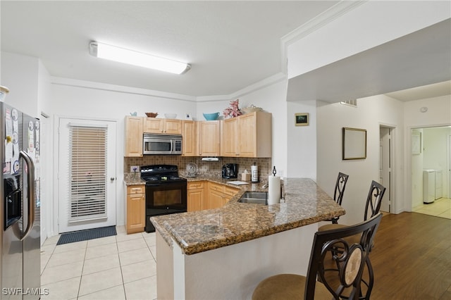 kitchen featuring a breakfast bar, light brown cabinetry, tasteful backsplash, stainless steel appliances, and a peninsula