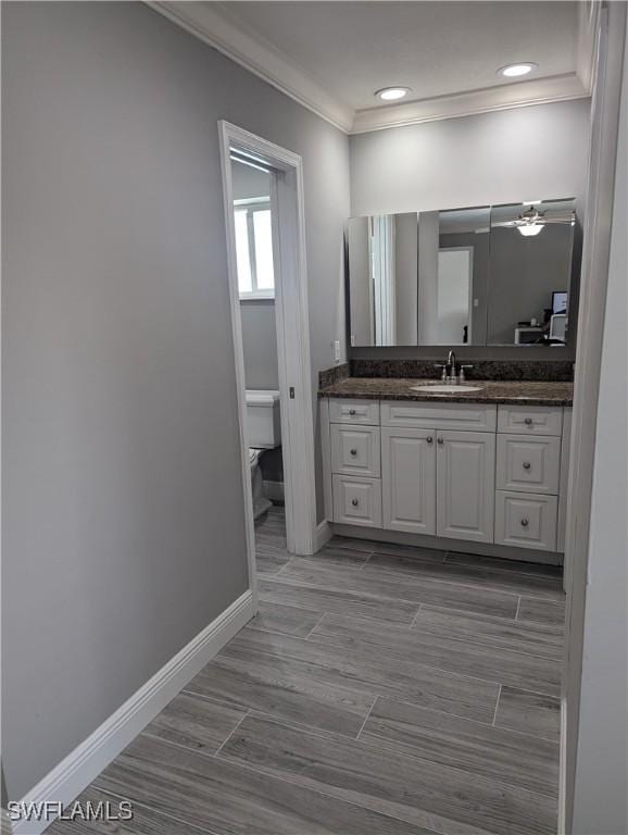 bathroom with baseboards, toilet, ornamental molding, vanity, and a ceiling fan