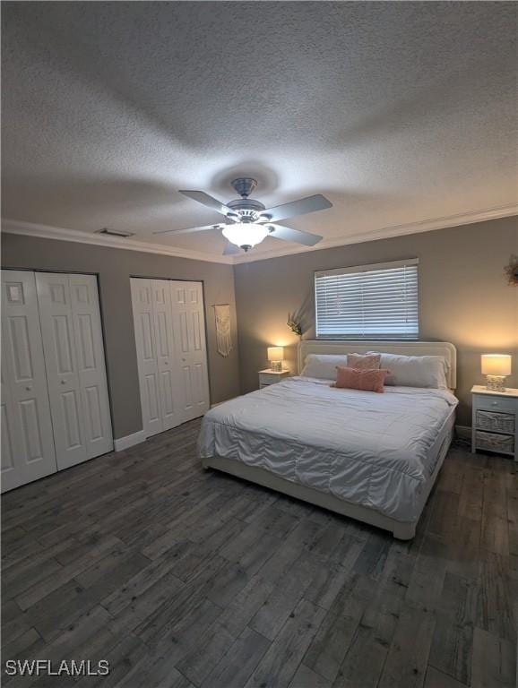 bedroom featuring wood finished floors, visible vents, ornamental molding, a textured ceiling, and two closets