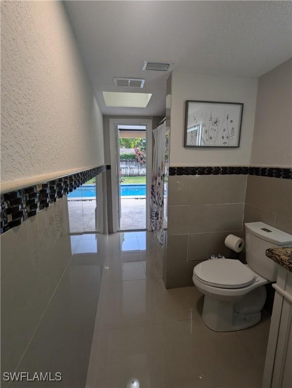 bathroom with tile patterned flooring, visible vents, a wainscoted wall, toilet, and vanity